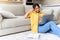 Charming and calm African-American woman sits on the floor in cozy living room with a laptop, enjoys lazy weekend in