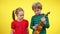 Charming Caucasian brother and sister playing ukulele at yellow background. Portrait of positive playful children with