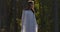 Charming Caucasian girl standing in sunlight in the forest and looking to the side. Beautiful woman in light white dress