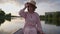 Charming Caucasian trans woman in pink dress and straw hat sitting in boat on lake looking away. Portrait of confident