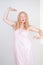 Charming chubby blonde girl in pink pretty nightgown stretch hands on white background in Studio