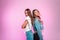 Charming cute positive girlfriends in trendy spring jeans clothes posing near bright pink wall indoors. Beautiful women in