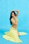 Charming dancer performs oriental belly dance on a blue background. A girl in a yellow beautiful dress is dancing an oriental bell