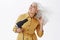 Charming elegant grandmother with grey hair standing in trendy yellow coat bending right, making last preparations to go