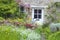 Charming english cottage with white doors, flowers in the garden