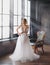 Charming excellent lady became bride, girl with blond gathered hair tries on wedding chic white luxurious light dress in