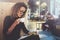 Charming fashionable woman with eyes glasses in a black sweater sits at a table in a cafe at night and reading book