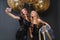 Charming fashionable young women in luxury black dresses making selfie with big balloons with golden tinsels on black
