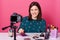 Charming female blogger sits at table with lots cosmetics products, records tutorial video ,looks at her digital camera. Smiling