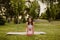 Charming fit young woman is sitting on knees on sports mat with rubber small pilates ball in park