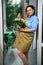 Charming florist holding a wicker basket with orchids for special festive event, standing at the entrance of flower shop