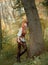 Charming forest robber rests leaning against a tree in the autumn orange forest. a lovely girl with bright red hair