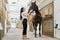 Charming girl is going to groom purebred stallion at stable