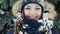 A charming girl with snow on her hair and head looks at the camera in a snowy forest