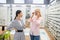 Charming girl wearing stylish earrings helping woman to choose glasses frame