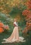 Charming gorgeous girl with fiery red hair stands alone in autumn forest in long light chic dress dress, holding cute