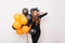 Charming graceful girl in witch hat holding helium balloons. Indoor shot of blithesome brunette lady in long dress