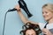 Charming hairdresser lady drying client`s brown hair on rollers over blue