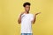 Charming handsome young black man holding his hand up to show present sell product. Isolated over yellow background.