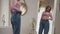 Charming happy female in oversized jeans demonstrating successful diet plan in front of mirror