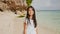 A charming and happy philippine teenage girl in a white summer dress is running along a tropical beach near the rocks