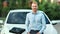 Charming happy positive young business man posing outdoor looking at camera sitting on car bonnet