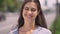 Charming happy young woman smiling with teeth and looking at camera, standing on street near road