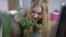 Charming hipster millennial woman looking at plant in pot smiling. Portrait of relaxed happy Caucasian employee in