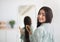 Charming Indian woman with long beautiful hair standing with wooden brush in front of mirror, looking at camera indoors