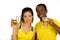 Charming interracial couple wearing yellow football shirts, posing for camera holding beer glasses and smiling, white