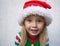 Charming joyful toddler girl in a Santa hat and an elf jacket lies on a light background. Festive mood