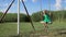 A charming little blonde girl is swinging at a green field.