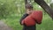 Charming little boy boxing gloves punches in big red gloves and stands outdoors in a park or garden wearing black jacket