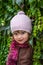 Charming little girl child in a hat and coat standing against the wall with wild grapes sunny autumn day playing and enjoying