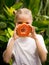 Charming little girl with fresh papaya. Caucasian girl holding slice of papaya fruit in front of her face. Selected focus. Green