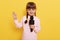 Charming little girl with pigtails looking at camera and holding microphone, cute artist isolated over yellow background with