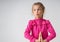 Charming little girl stands clasping hands, looking aside and funnily pursing her lips . Waist-up studio shot isolated