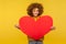 Charming lively energetic woman with fluffy curly hair holding big heart love symbol, looking at camera