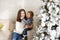 Charming mother in the white sweaterholding her little toddler son near Christmas tree in the house