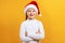 Charming portrait of a happy cute little girl in santa hat. The child crossed his arms and looks at the camera.