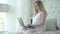 Charming pregnant woman typing on laptop keyboard and smiling. Side view portrait of happy Caucasian expectant messaging