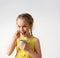 Charming preschool girl in yellow dress with braided hair eating yoghurt with great pleasure. Close up studio portrait