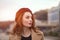 Charming pretty french woman in an autumn beige coat and red beret standing outdoors with urban city background. Tinted