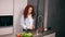 Charming red headed woman washing red pepper, cucumbers and tomato in kitchen and putting them on plate. Homemade food