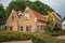 Charming rustic house with flowered garden, leafy trees and fence in a cloudy day at Drimmelen.