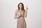 Charming sensual caucasian woman in glittering beige evening dress, showing victory or peace gestures, feeling confident