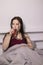 Charming sleepy brunette woman with glass cup of tea in bed with grey bed linens. morning routine