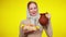 Charming slim cheerful rural woman posing with eggs and milk pot at yellow background. Portrait of joyful redhead