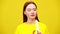 Charming slim redhead woman peeling and eating banana in slow motion at yellow background. Portrait of confident