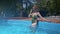 Charming slim woman is standing in shallow of pool, camera is moving to her face, she is smiling